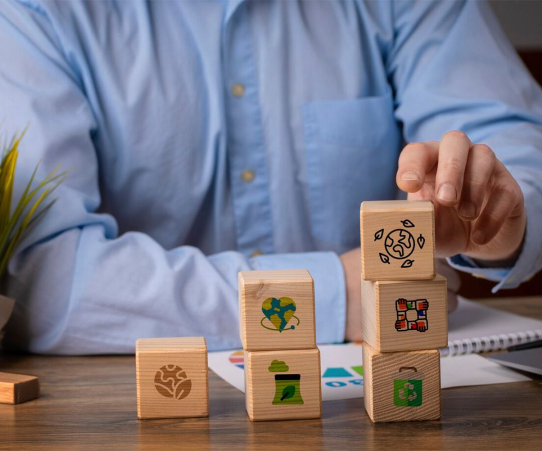 Persona apilando cubos de madera con iconos relacionados con la responsabilidad social y el medio ambiente.